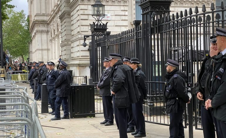 The upcoming election and Police officers standing guard outside a government building, with metal barricades and iron gates, maintaining security and order in a city setting.