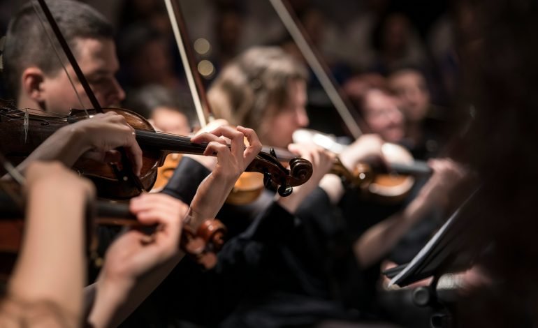 Close-up of musicians playing violins in a classical orchestra during a live performance.