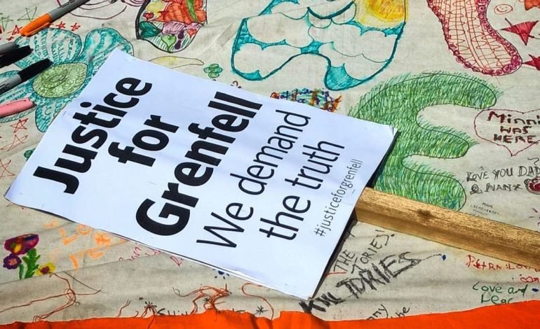 The image shows a sign that reads "Justice for Grenfell, We demand the truth" placed on a tablecloth with colorful drawings and messages. Residents from Lancaster West Estate demand answers regarding the refurbishment and rising costs