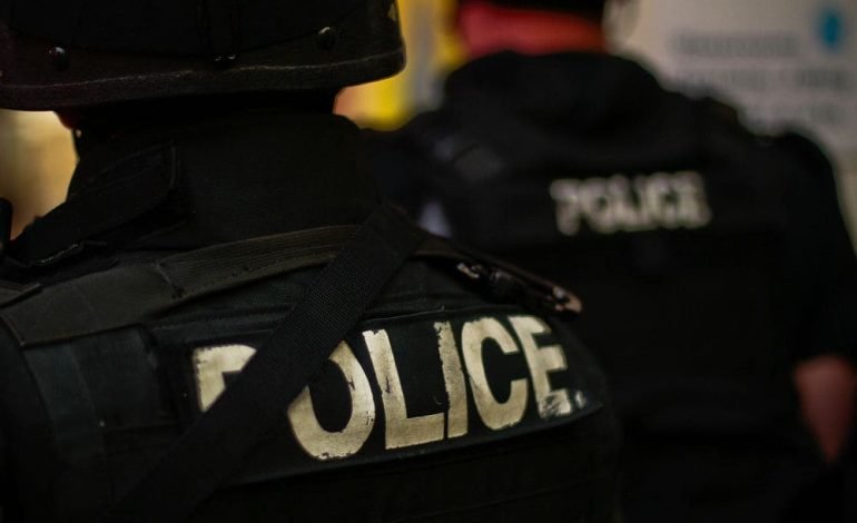 Back view of two police officers in tactical gear with 'POLICE' written on the back of their uniforms, during a response to an incident in Ladbroke Grove.