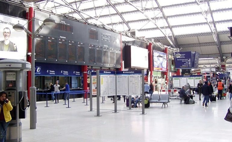 Inside London Liverpool Street Station, with passengers walking and waiting, information boards, and ticket counters visible