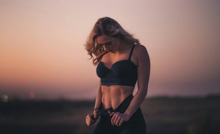 Woman wearing a sports bra outdoors at sunset, adjusting her jeans