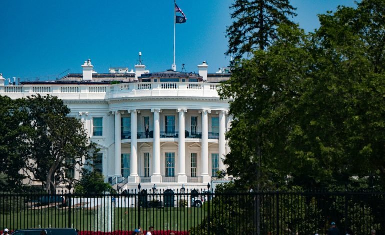 The White House in Washington, D.C. with an American flag flying on top, highlighting the setting of recent internal turmoil and scrutiny within the Biden administration.