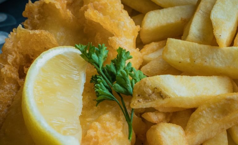 Classic British fish and chips served with a lemon wedge and mushy peas, highlighting the traditional meal's increasing cost due to rising potato prices.