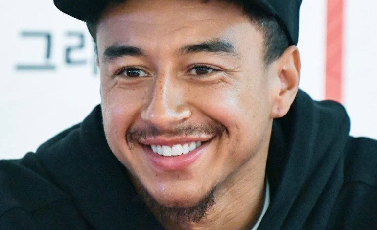 Jesse Lingard's move shows him smiling and wearing a black cap with his name, Jesse Lingard, during a fan event