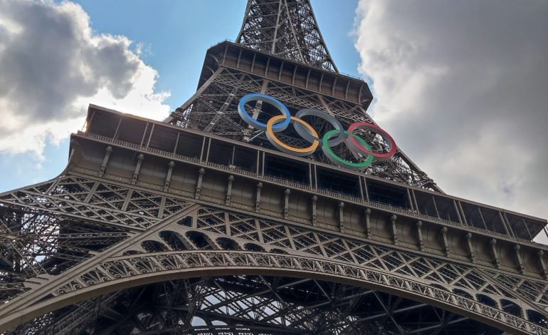 The Eiffel Tower adorned with the Olympic rings against a backdrop of a partly cloudy sky, symbolising the Paris 2024 Olympics.