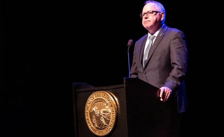 Minnesota Governor Tim Walz speaks at a podium, representing the positive and optimistic tone of the Harris and Walz campaign.