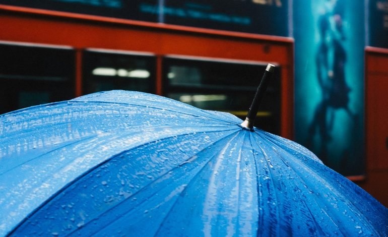 Blue umbrella in rain under yellow weather warning, reflecting heavy rain forecast in southern UK.
