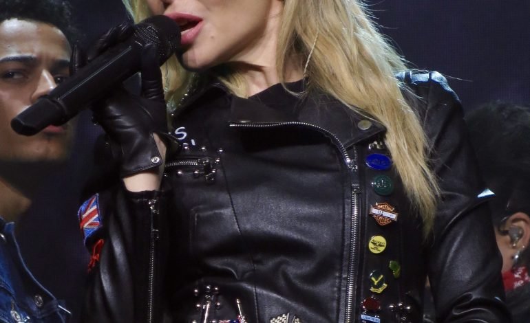 Kylie Minogue performing live, wearing a black leather jacket, during her world tour.