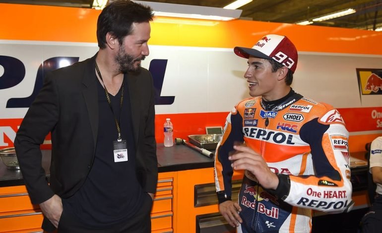 Keanu Reeves makes a connection with a Repsol Honda rider at a motorsport event.
