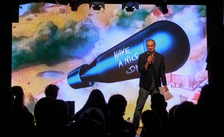 Comic Strip legend on stage at The Phoenix Arts Club in Soho with iconic 'Have a Nice Day' bomb backdrop.