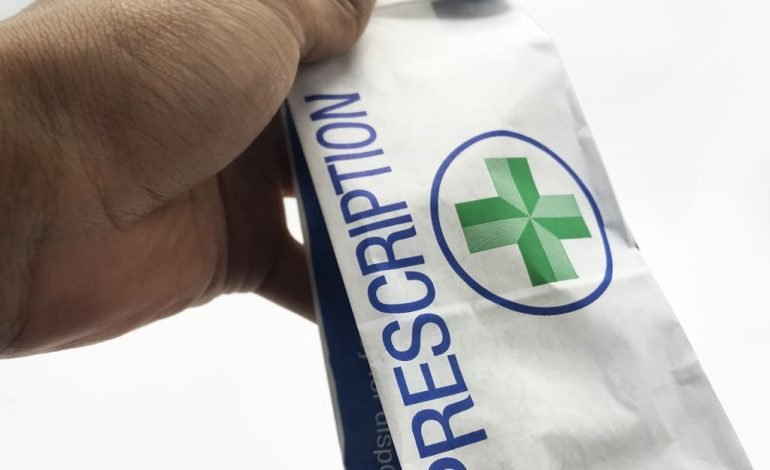 Prescription bag held by hand, symbolising UK pharmacies' services amidst funding challenges.