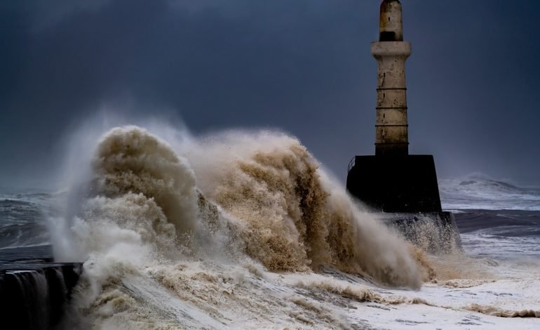 Storm Conall waves crashing against a lighthouse during heavy rain and strong winds in the UK.