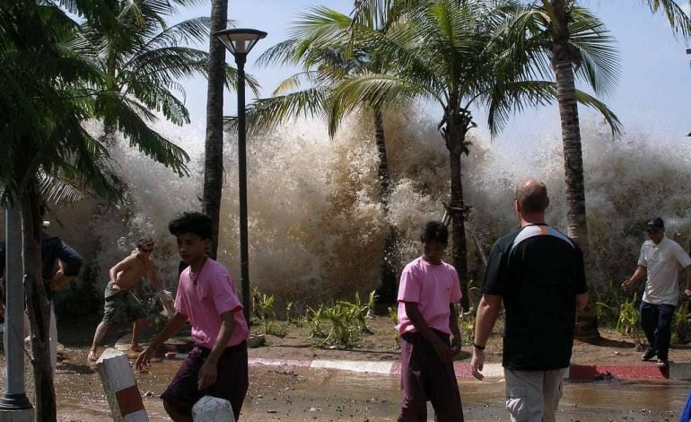 People flee as the 2004 Indian Ocean tsunami wave crashes ashore, a stark reminder of the disaster's devastating impact.