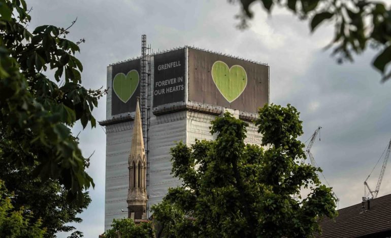 Grenfell Tower covered in protective sheeting with a green heart memorial, as plans for its demolition move forward in London.