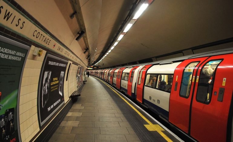 London Underground train stopped at Swiss Cottage station, showing the curved platform and station signage.