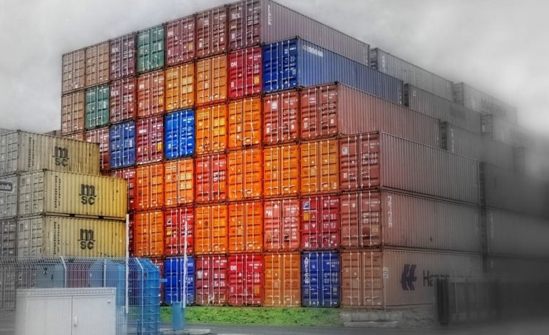 Stacked shipping containers at a port as U.S. imposes tariffs on Canada and Mexico, affecting global trade and supply chains.
