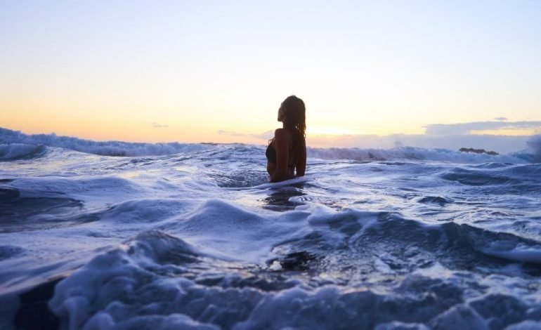 Woman in the ocean at sunset, representing the Global Happiness Megastudy's exploration of wellbeing and happiness across different lifestyles.