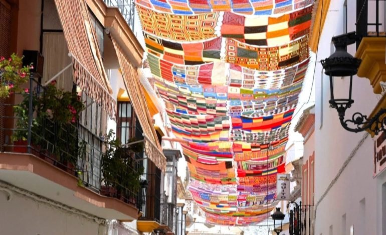Crocheted canopies stretching across a narrow street in Arahal, Spain, creating colourful shade with handmade textile panels.