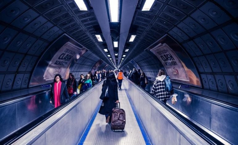 Passengers with luggage in a London Underground tunnel, highlighting the potential impact of the London tourist tax on city visitors