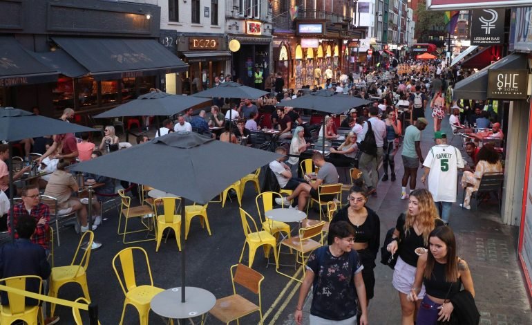 People enjoying alfresco dining in Soho with closed streets and outdoor tables during a summer evening