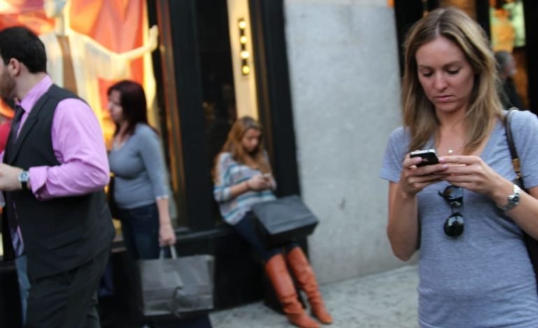 Woman using smartphone on a busy London street as part of London phone theft awareness focus
