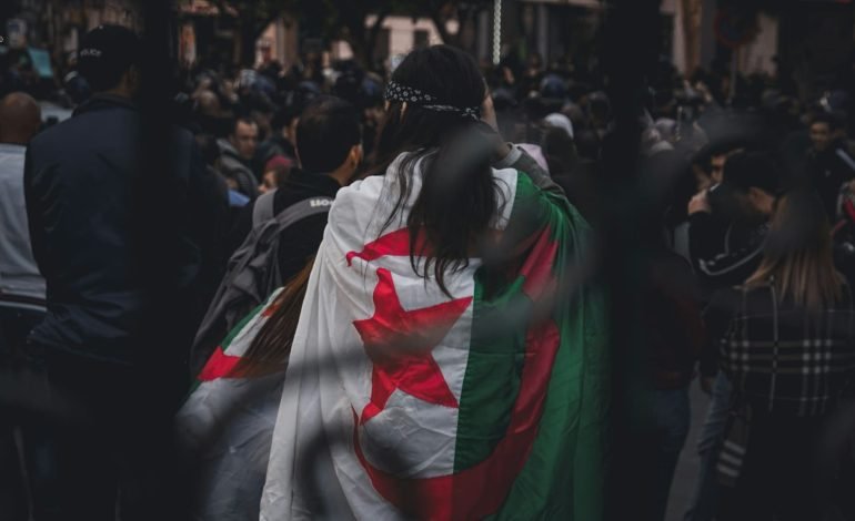 group of people with woman in the middle draped in Algeria flag
