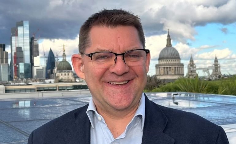 Brendan Barns smiling on a rooftop in the City of London with St Paul’s Cathedral and skyscrapers in the background