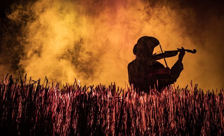 Fiddler on the Roof Barbican production with Raphael Papo silhouetted as the Fiddler against wheat field and orange stage lighting