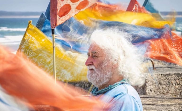 Man standing among silk pennants at Beach of Dreams UK art festival on a coastal promenade