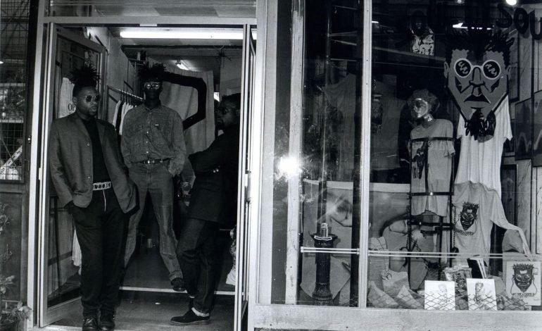Streetwear store associated with Black British music heritage, with three men outside and graphic t shirts on display in 1980s London