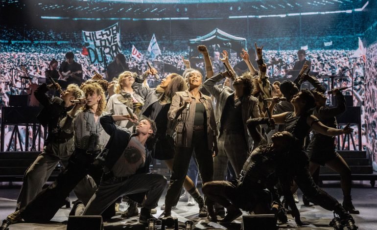 The cast of Just For One Day – The Live Aid Musical performing on stage with Wembley crowd backdrop. Photo credit Evan Zimmerman.