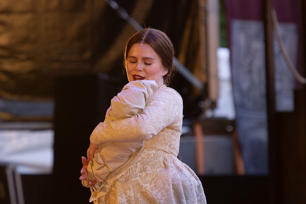 Anne Boleyn The Musical review – Emily Lane as Anne Boleyn at Hever Castle outdoor theatre, holding a swaddled baby