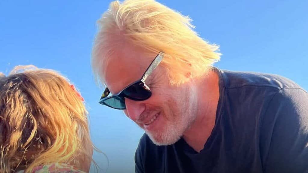 Boris Johnson beard on family holiday in Greece, smiling in sunglasses beside his child under a clear blue sky