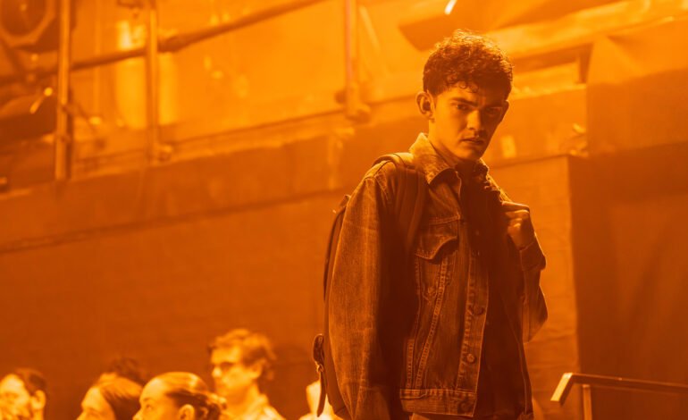 Actor as Jake in Clarkston at Trafalgar Theatre, West End, denim jacket, orange stage lighting, coming of age drama, night shift Costco scene