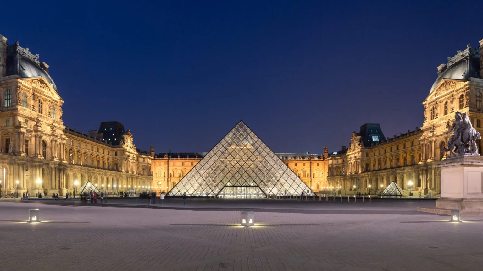 Louvre Museum Paris courtyard at night with illuminated glass pyramid following the Louvre heist and renewed focus on museum security.