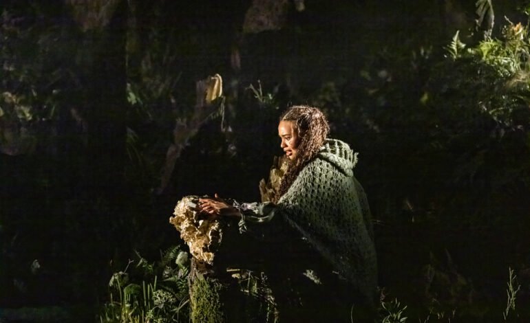 Into the Woods at the Bridge Theatre London, with a performer framed by the forest set during a quiet, reflective moment in the production | Image Credit Johan Persson