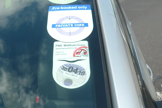 TfL licensing delays compensation highlighted by private hire licence discs displayed on a London vehicle windscreen