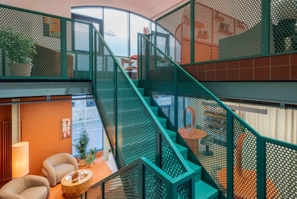 The sculptural staircase inside Blue Tit Battersea, where perforated green steel, warm cork flooring and soft seating create a calm, considered space designed to slow the pace of a salon visit.