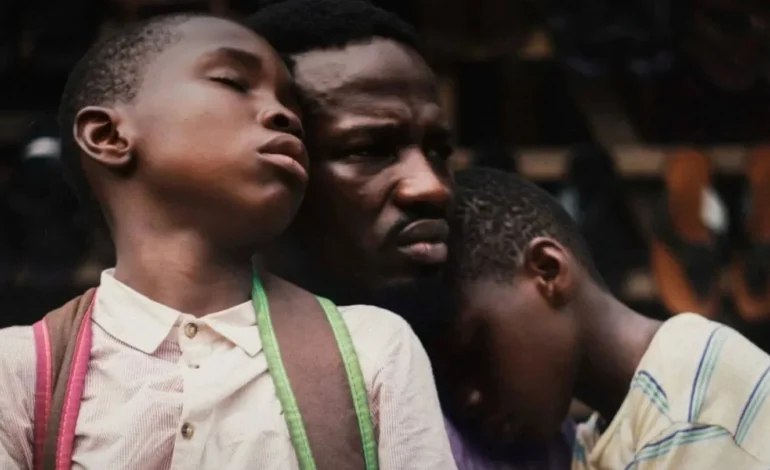 My Father’s Shadow film still showing Sope Dirisu with two young boys during a tense moment in 1990s Lagos.