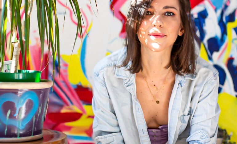 Chess column writer Daniela seated in front of colourful artwork reflecting her art and chess practice