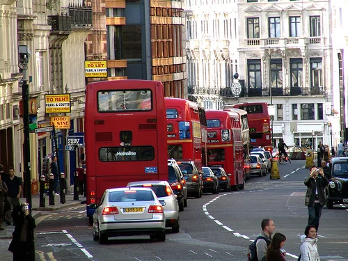Red London buses on busy city street as London bus fares innovation funding is announced by City Hall