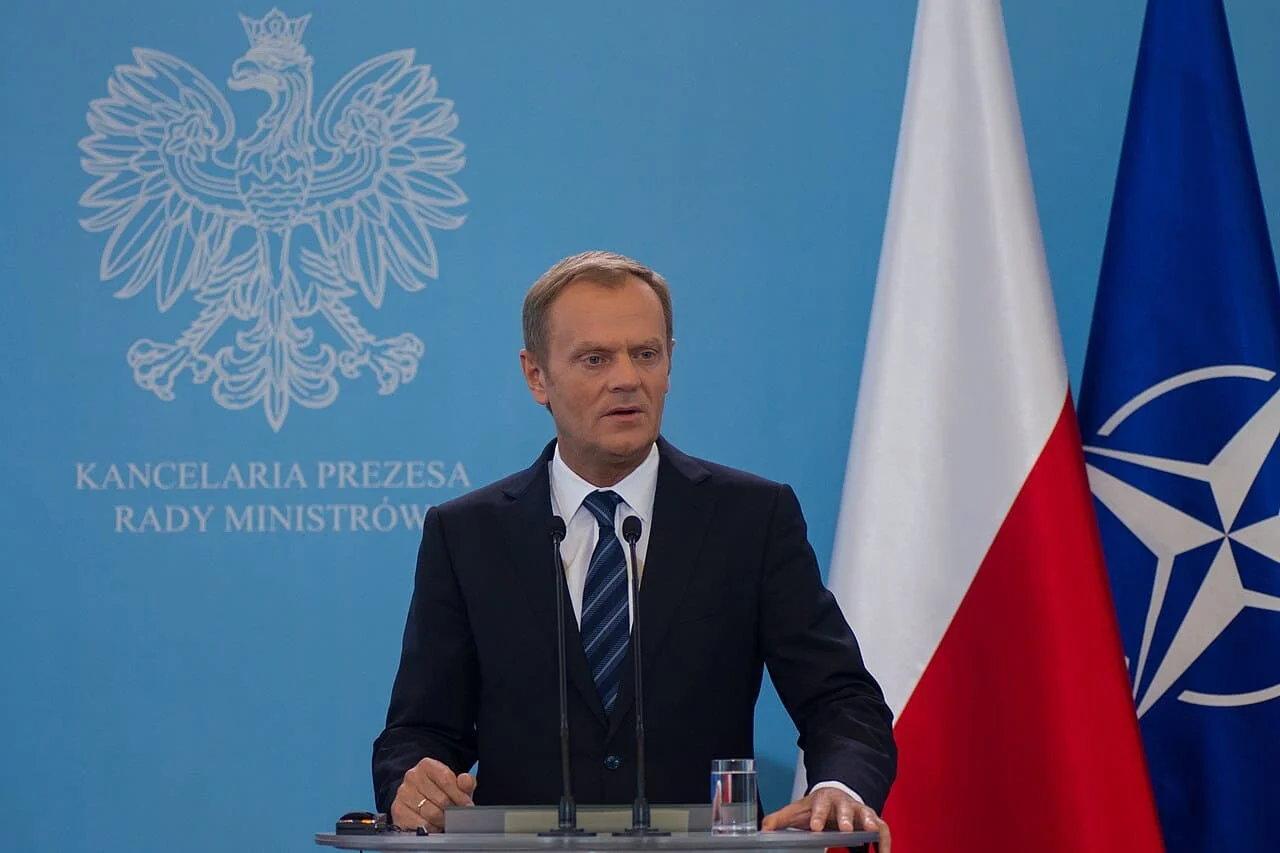 polish pm donald tusk with a lectern and poland and nato flags behind him
