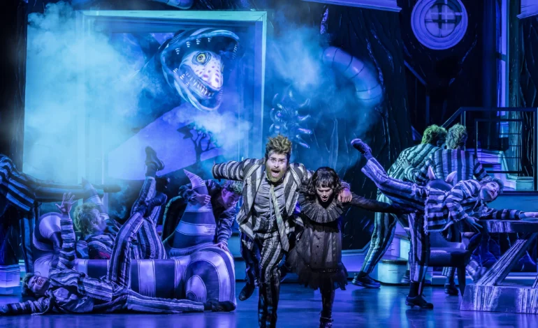 David Fynn as Beetlejuice and Hannah Nordberg as Lydia Deetz, surrounded by the company in a stage scene from Beetlejuice the Musical