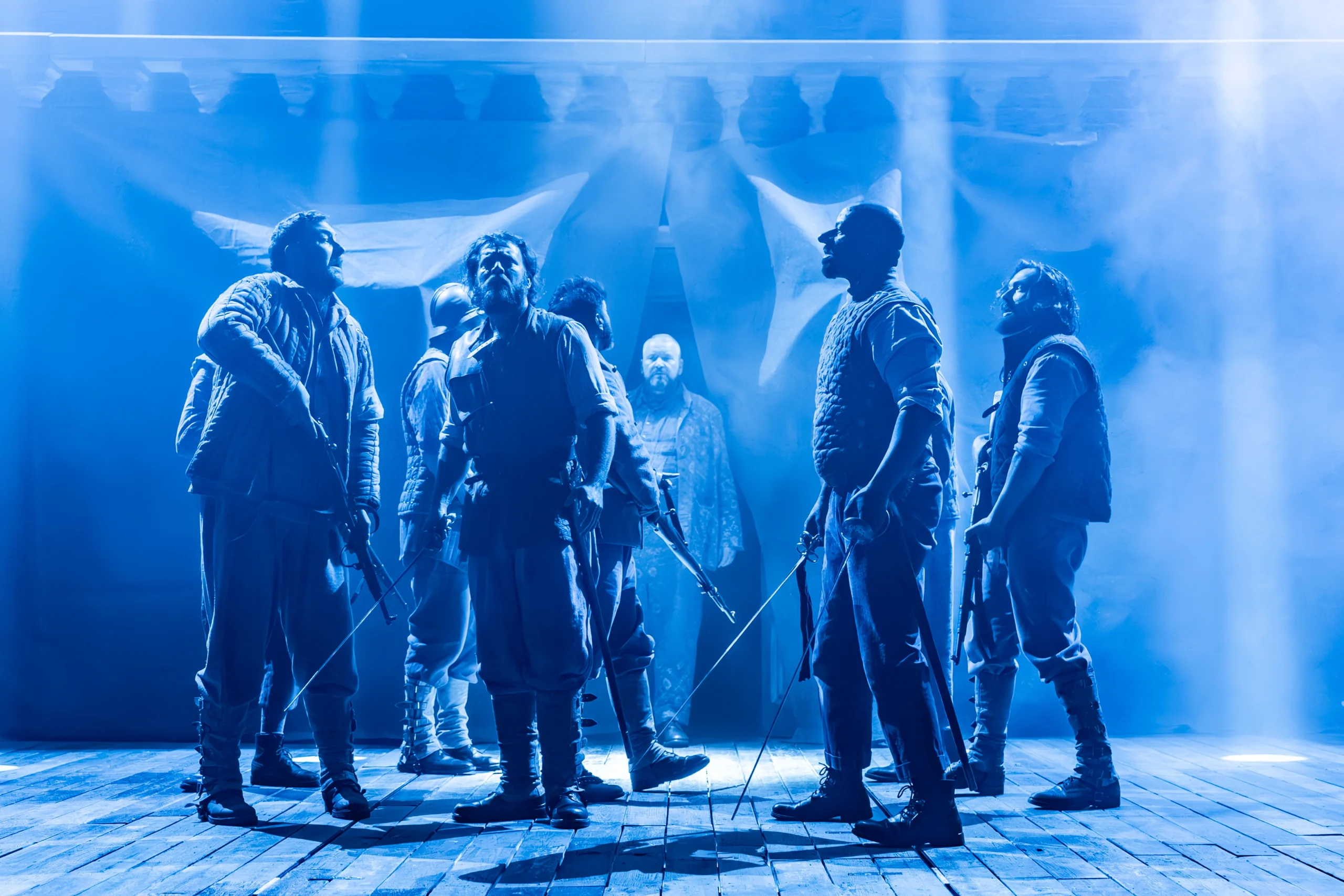 Cast of Cyrano de Bergerac in a tense blue lit stage scene at the Noël Coward Theatre