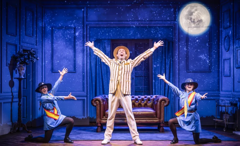 Sam Harrison as Bertie Wooster with two girl guides in Jeeves Takes Charge at Charing Cross Theatre