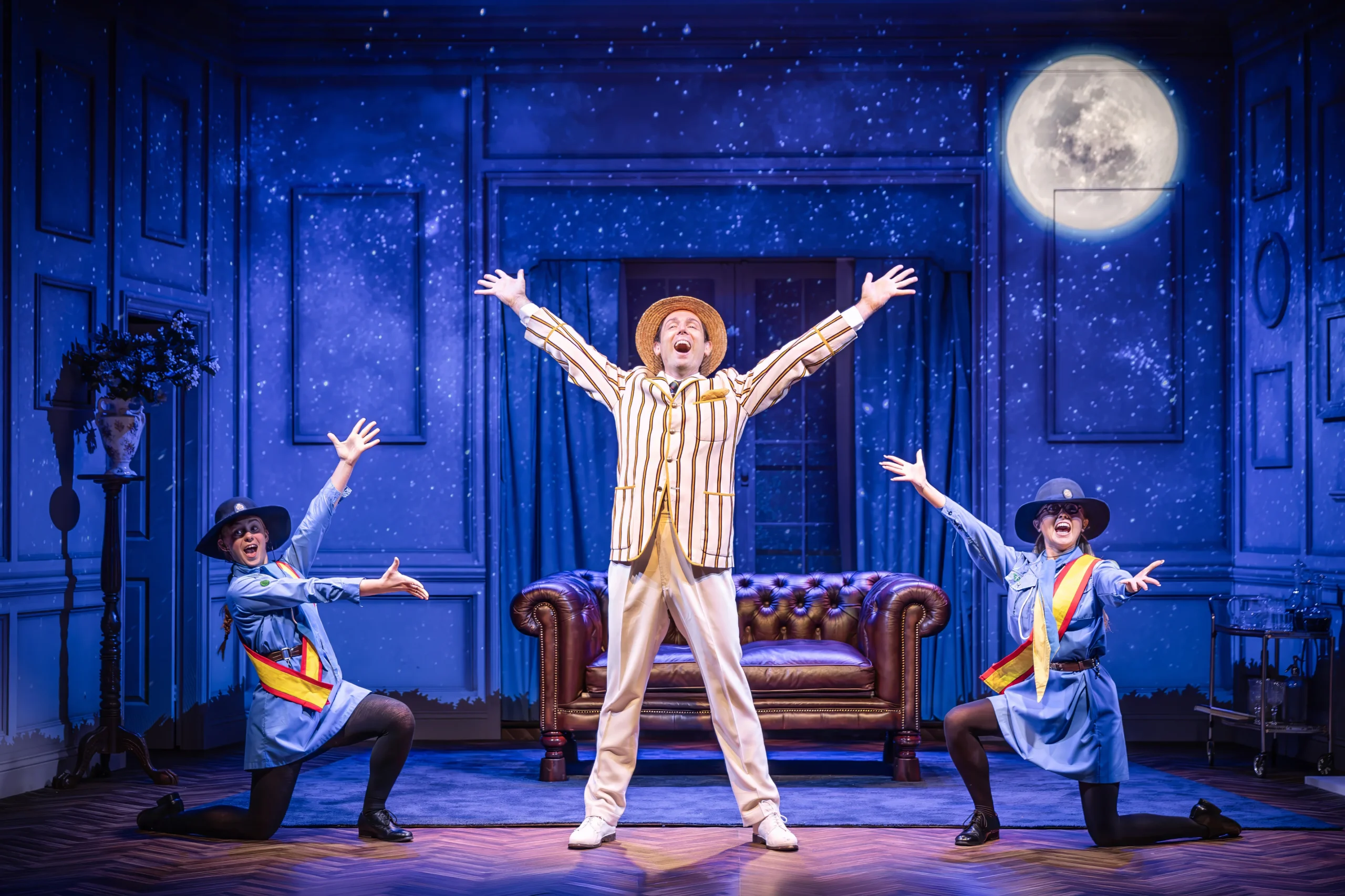 Sam Harrison as Bertie Wooster with two girl guides in Jeeves Takes Charge at Charing Cross Theatre