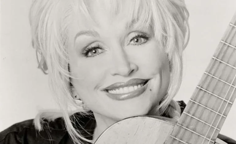 Dolly Parton smiles in a black and white portrait holding a guitar, star of Dolly Parton musicals
