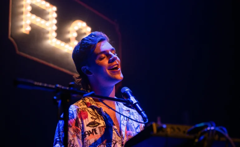 Arthur Hull performs Flop the musical cabaret beneath a lit FLOP sign at Wilton's Music Hall