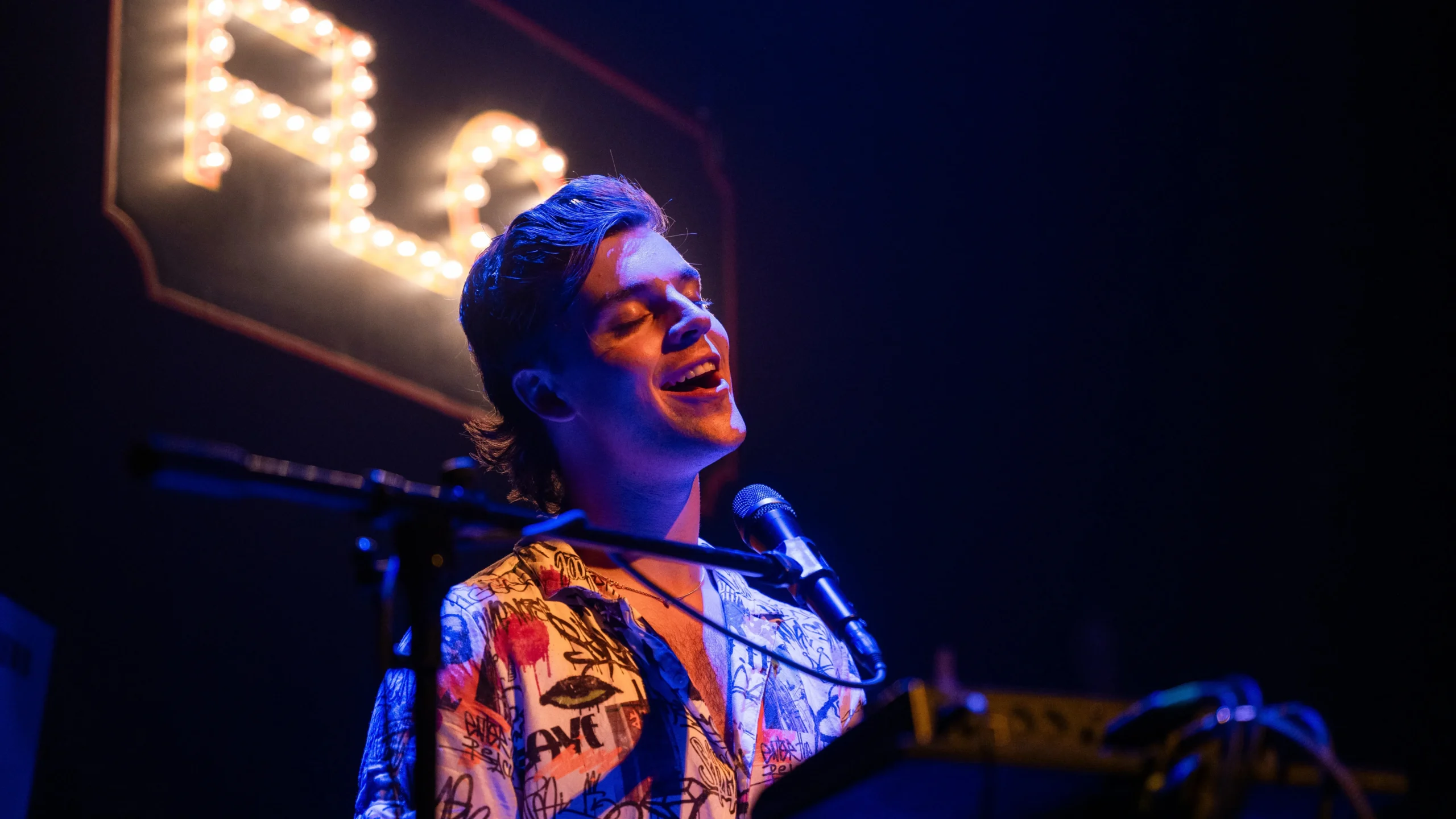 Arthur Hull performs Flop the musical cabaret beneath a lit FLOP sign at Wilton's Music Hall